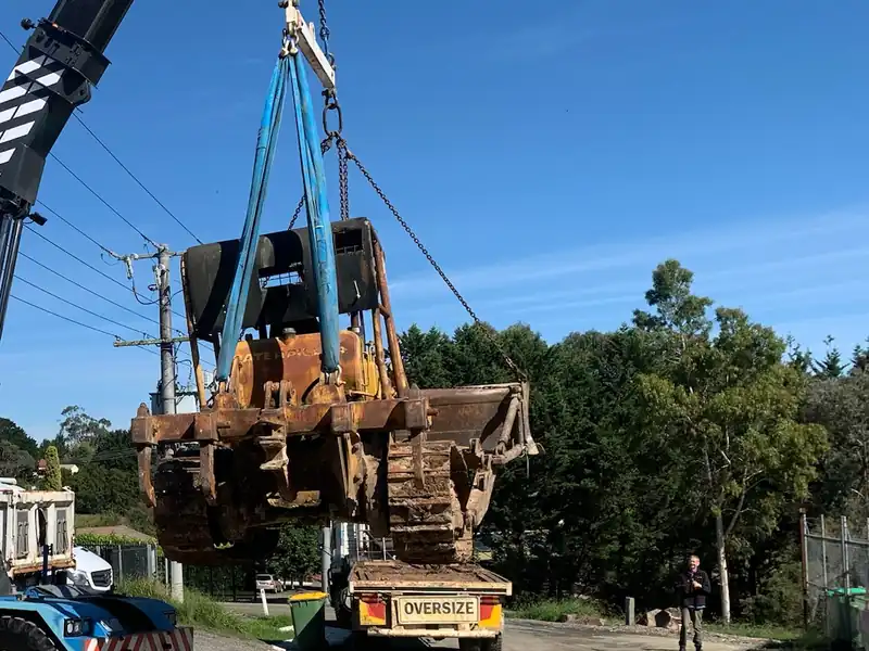 A bulldozer lifted on the crane hook above a road